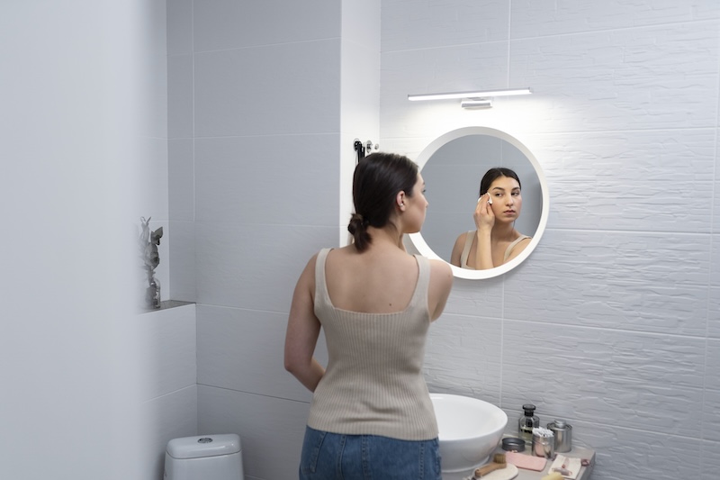 Femme qui se maquille devant son miroir de salle de bain